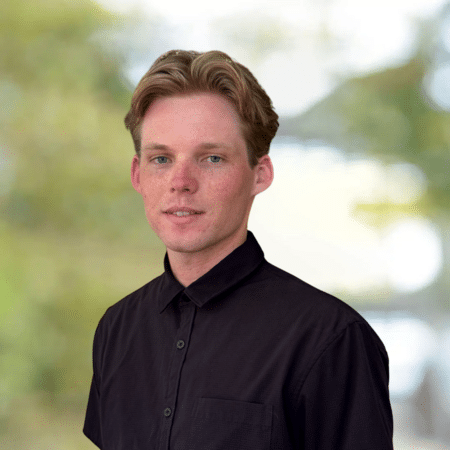 Portrait of Chase, a young man with blond hair, wearing a black button-down shirt. Professional headshot.